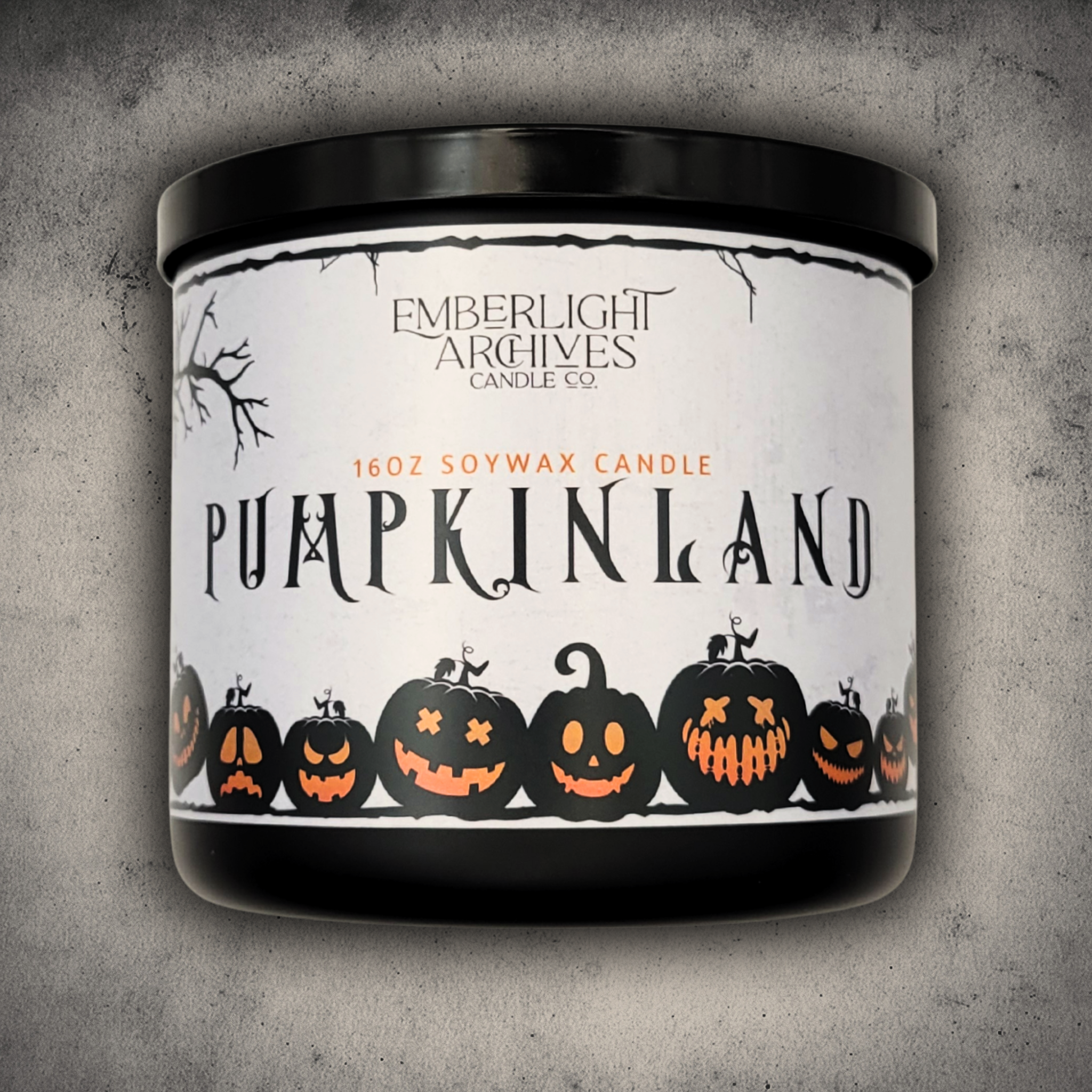 Emberlight Archives Pumpkinland candle in a 16oz black glass jar with whimical pumpkin label against a gray stone background.